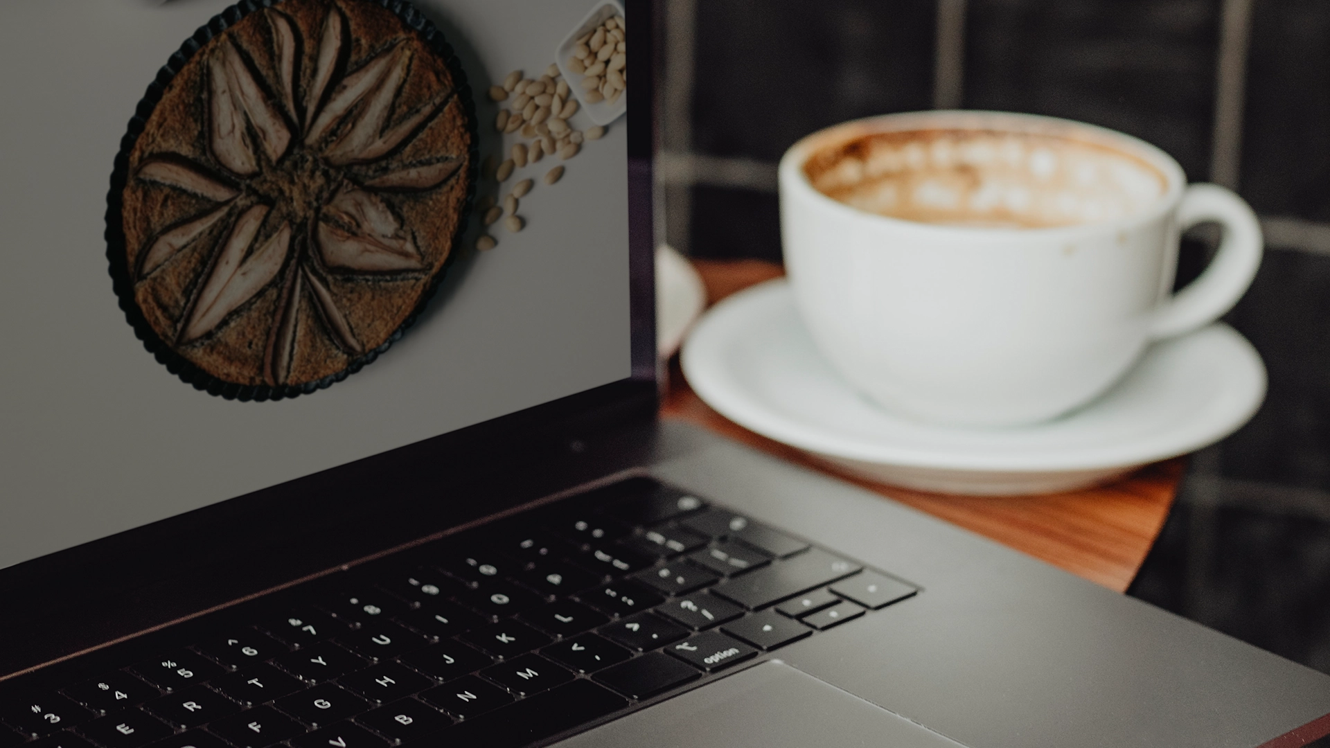 Laptop met een cappuccino ernaast op een houten bureau, tijdens het uitzoeken van de kosten voor een nieuwe website