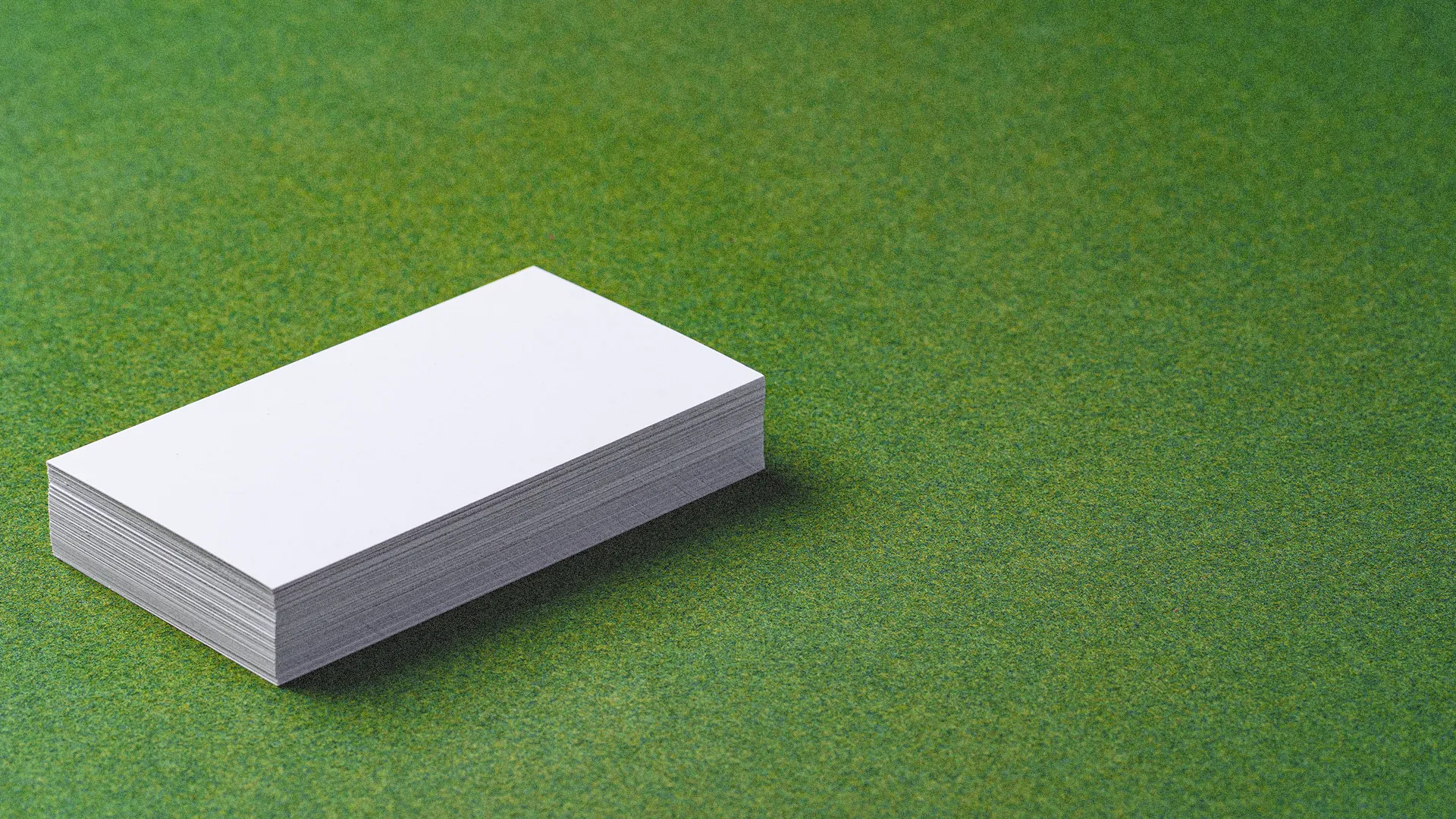 Stapel blanco witte visitekaartjes op een groene ondergrond, ter illustratie van de tastbare kracht van drukwerk