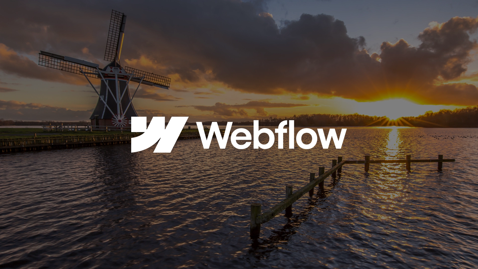 Het Webflow-logo over een Nederlandse molen bij zonsondergang aan het water