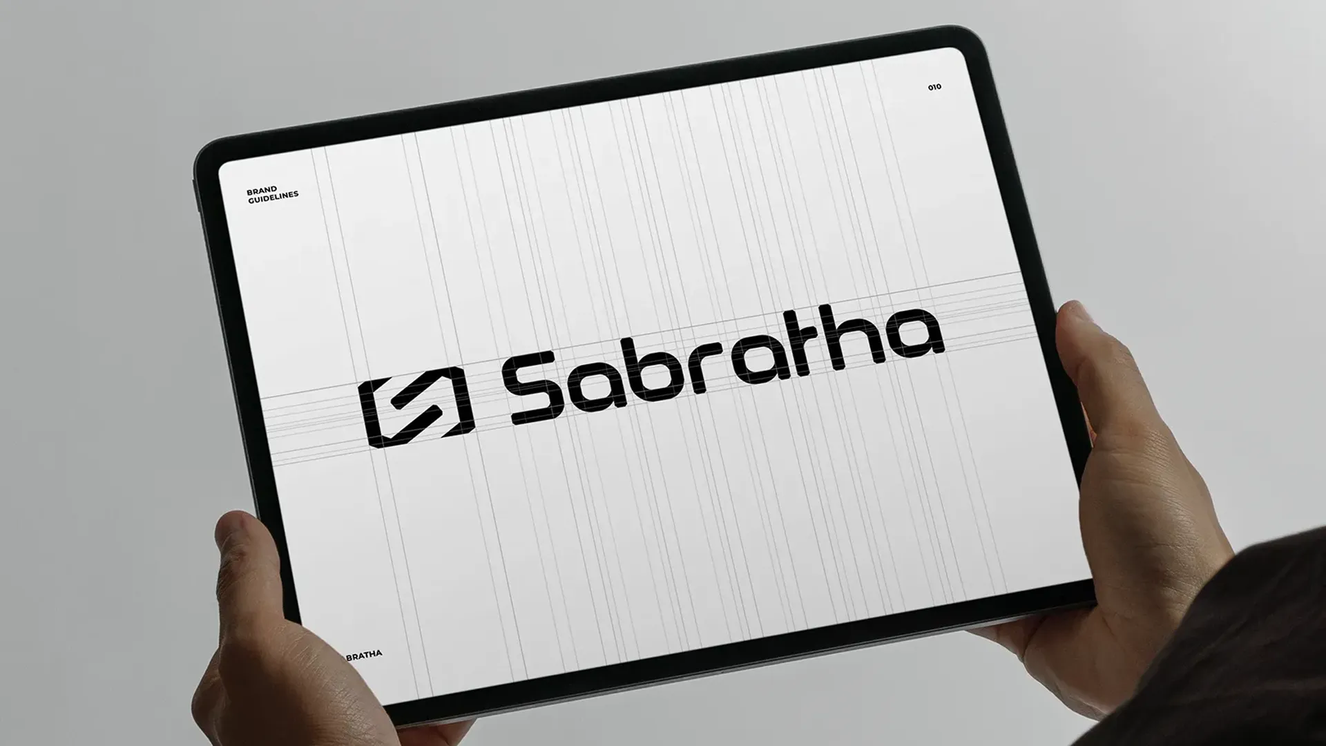 Iemand houdt een tablet vast met de brand guidelines van Sabratha erop, met het logo op een grid, een voorbeeld van wat een compleet brandingtraject oplevert