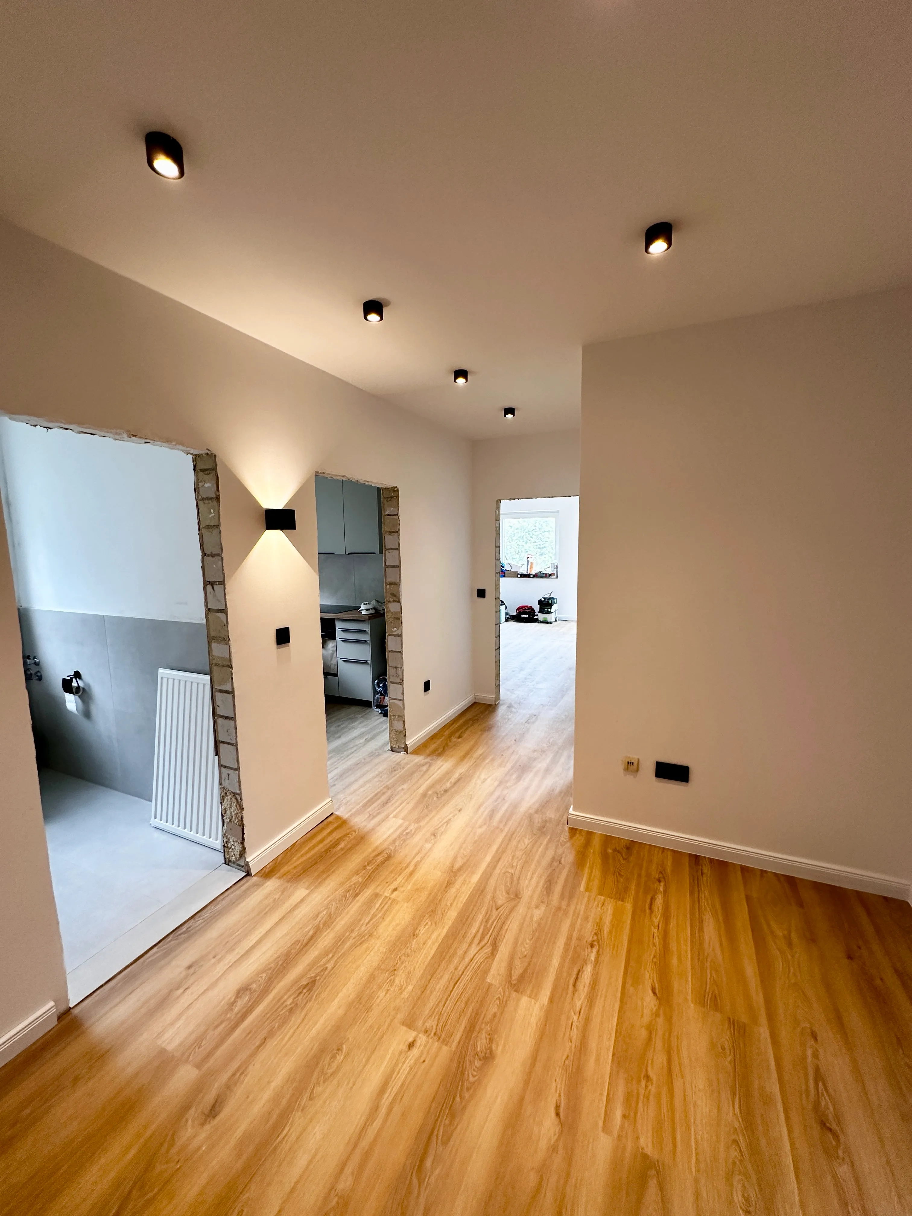 Modern sanierter Wohnungsflur mit hochwertigem Vinyl, weißen gespachtelten Wänden und Deckenspots.