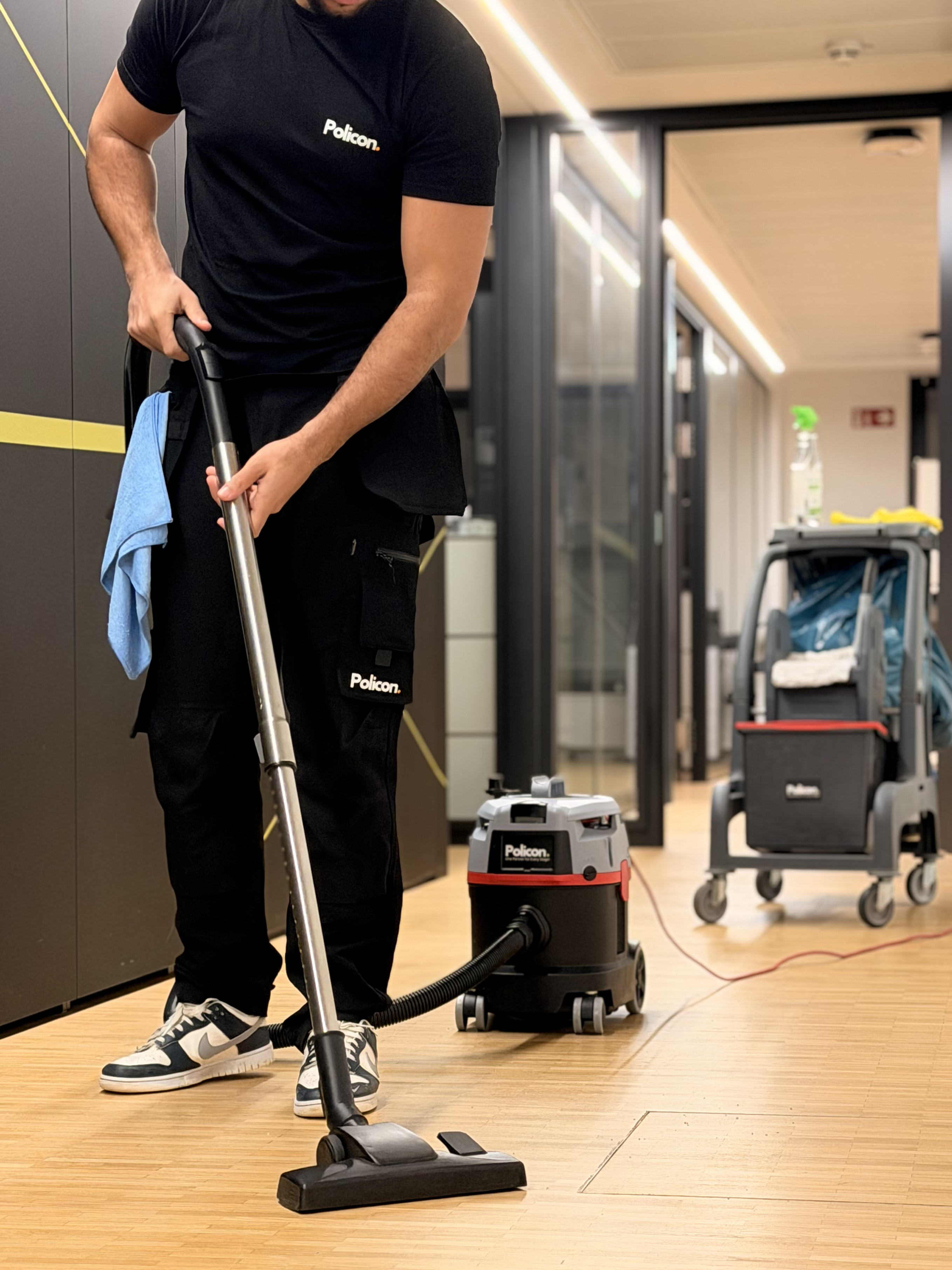 Mann in schwarzer Kleidung saugt den Holzboden eines Flurs mit einem Staubsauger der Marke Policon.