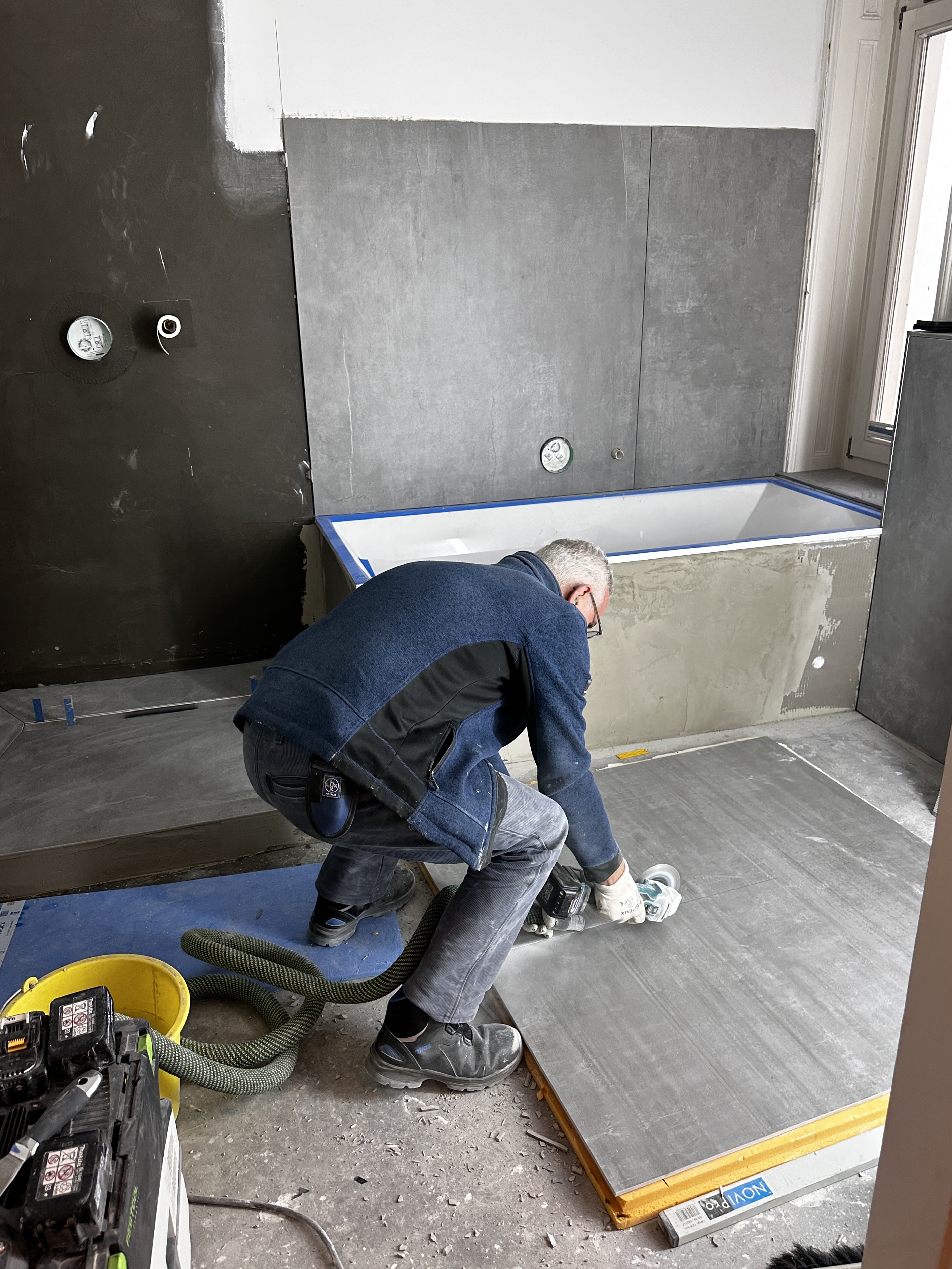 Handwerker schleift großen grauen Fliesenboden im Badezimmer mit einer Elektroschleifmaschine.