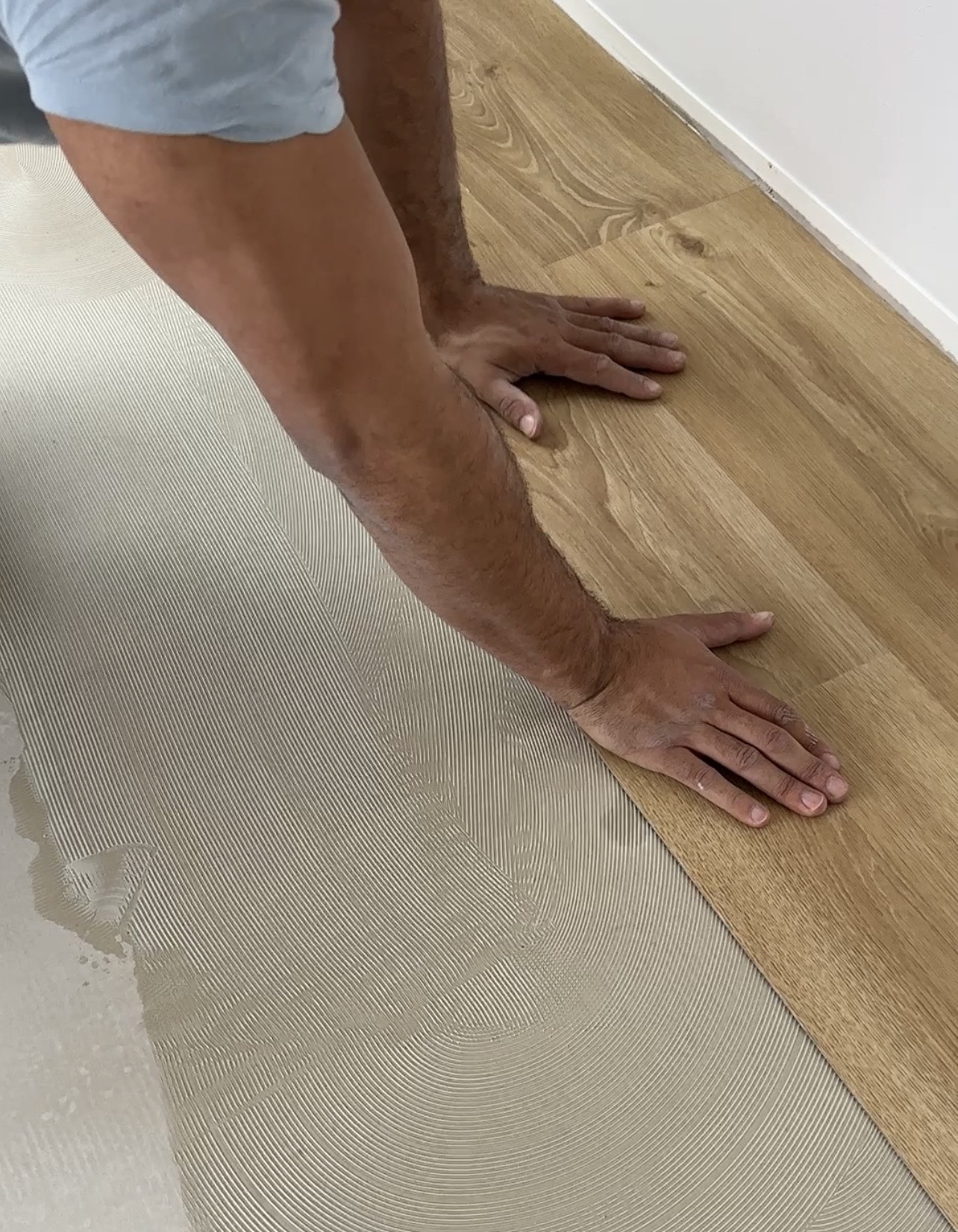 Person legt Holzboden auf einen Boden mit Kleber und glättet ihn mit den Händen.