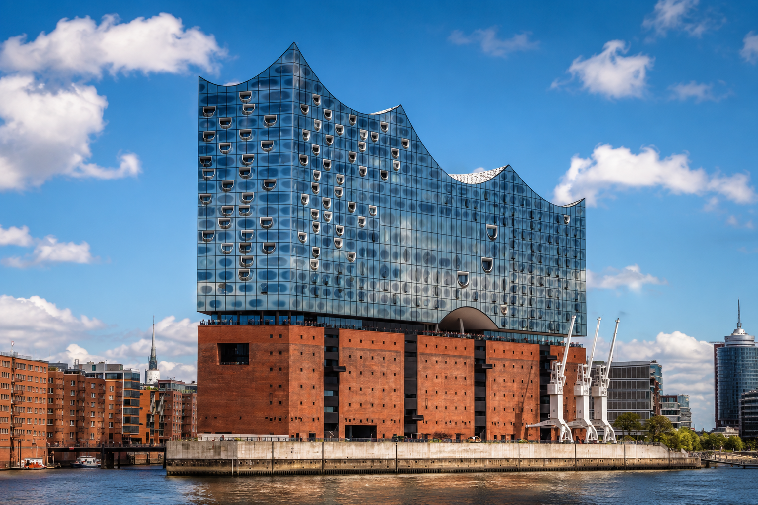 Die Elbphilharmonie in Hamburg mit ihrer wellenförmigen Glasfassade über einem roten Backsteinsockel am Ufer bei klarem Himmel.