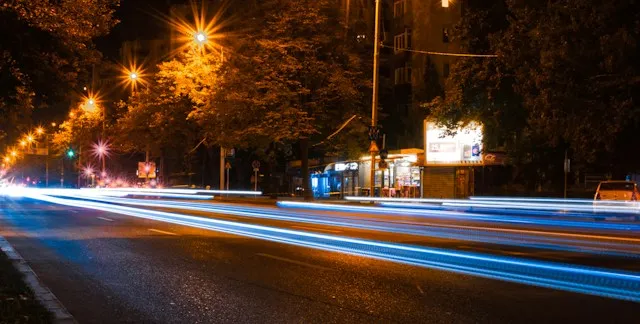 Nighttime city street with light trails from moving vehicles and illuminated street lamps.