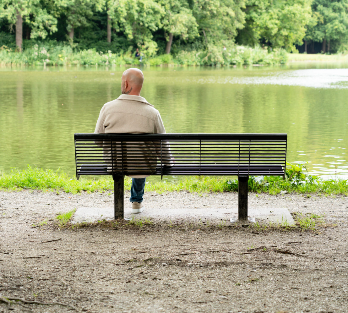 Jamel van ’t Hek zit alleen op een bankje bij het water, een rustige setting die past bij reflectie en zijn begeleidende werkwijze binnen Humanum Healthcare.