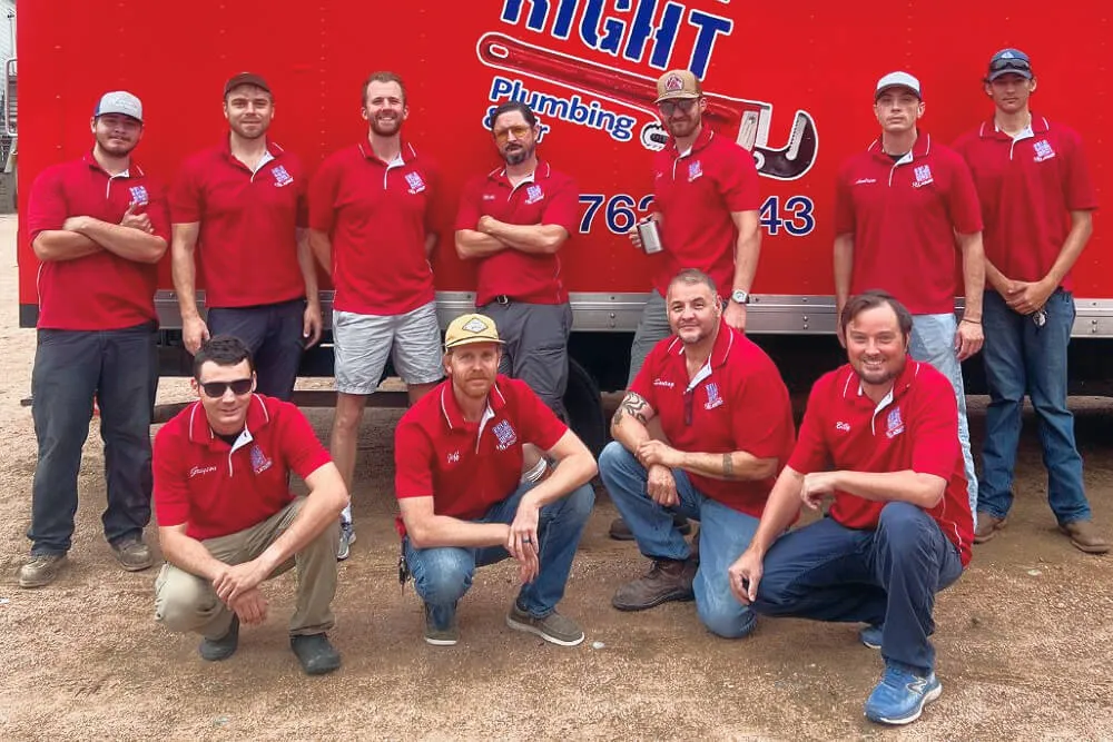 Group of ten plumbers in red shirts posing in front of a red company truck.
