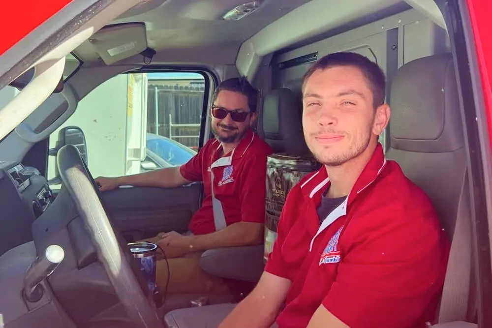 Two male plumbers in red shirts sitting inside a van.