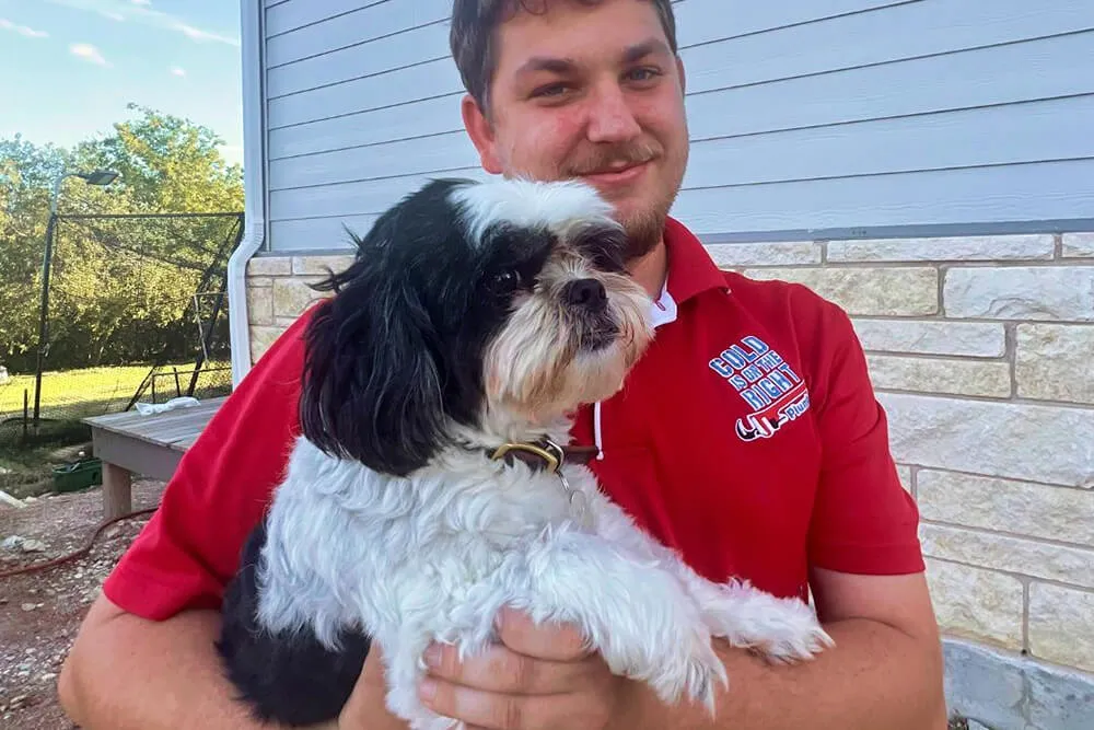 Man in red company shirt holding a black and white dog.