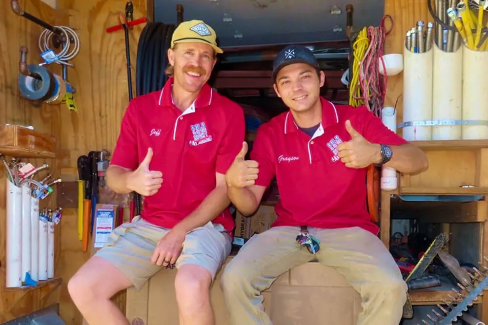 Two plumbers sitting, giving thumbs up.
