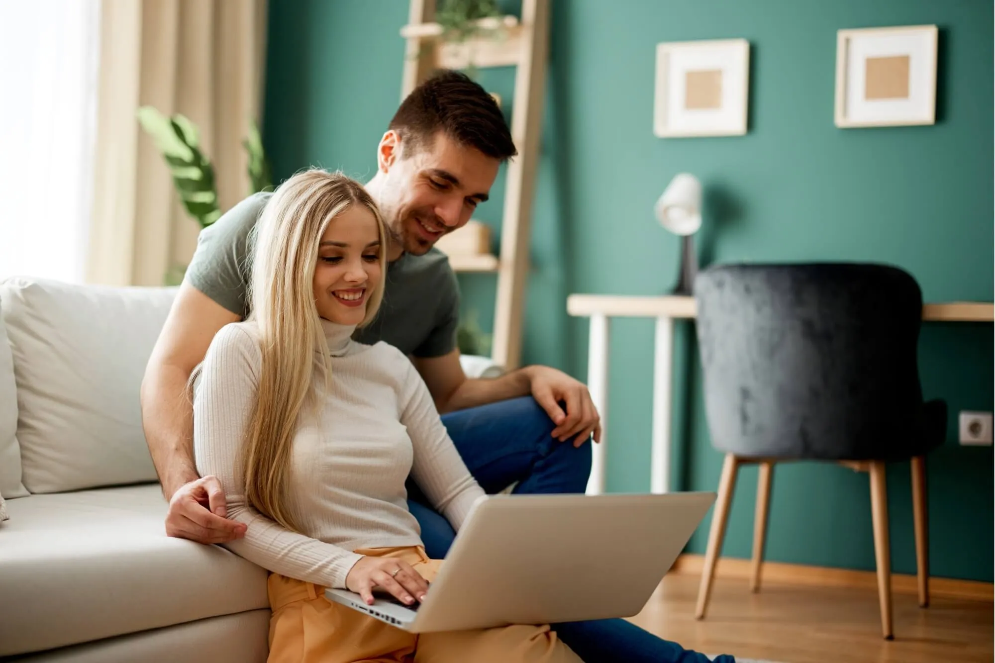 Couple comfortable and smiling at laptop on a sofa indoors.