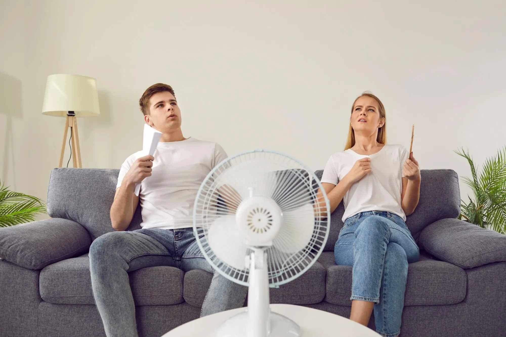 Couple fanning themselves with a table fan nearby.