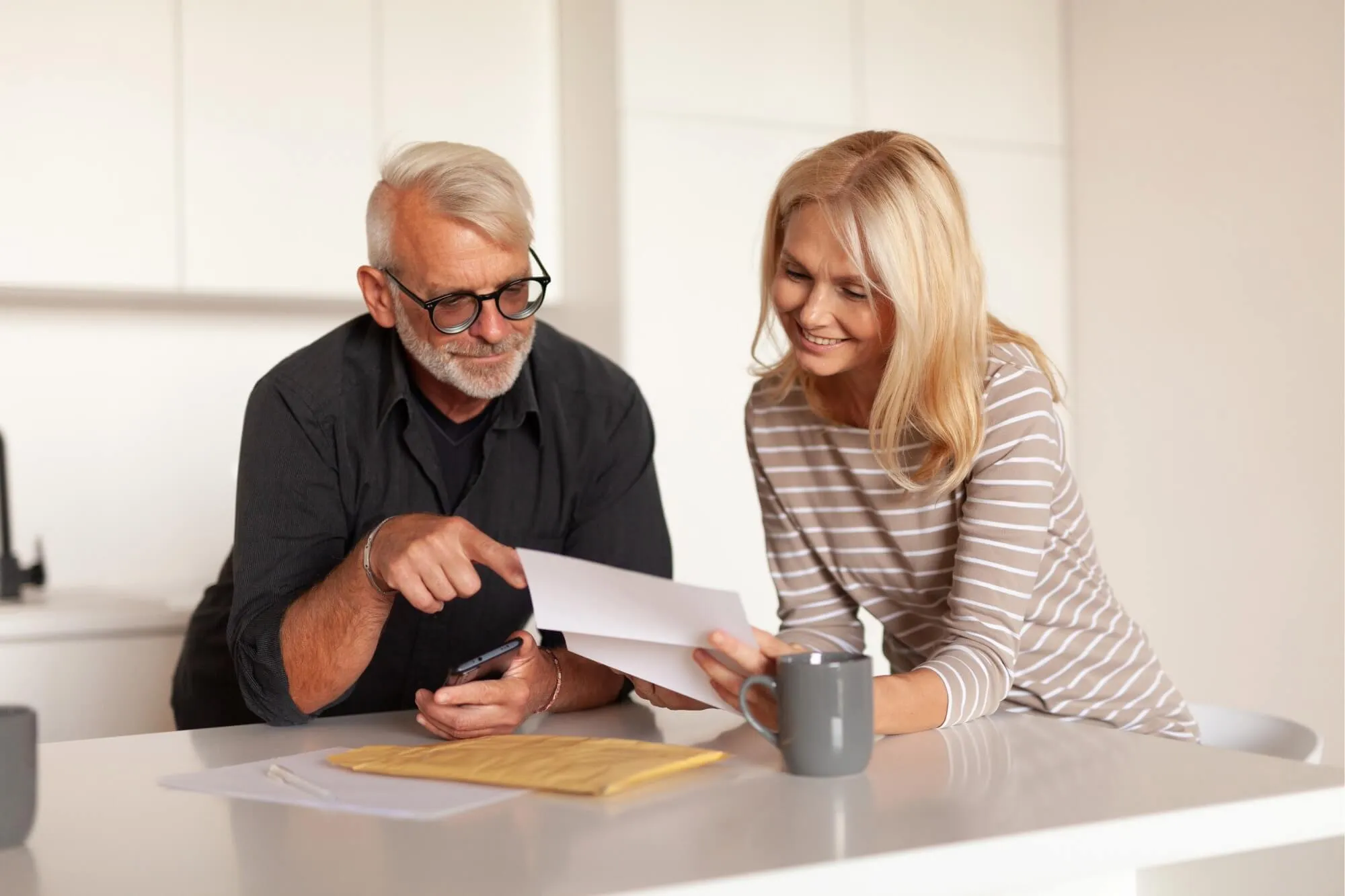 Older couple happily reviewing documents at kitchen counter.