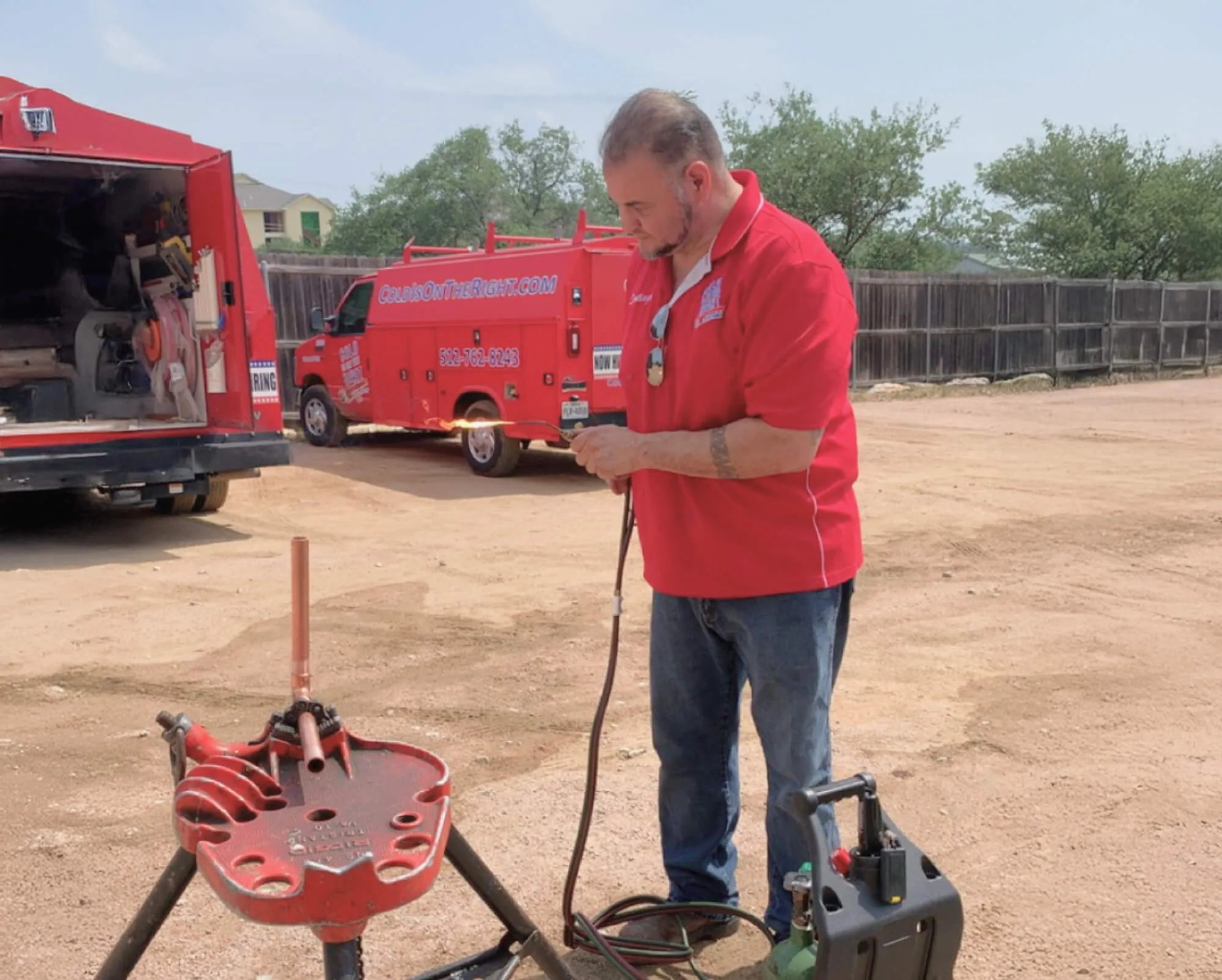 Plumber working outdoors next to red van and equipment.
