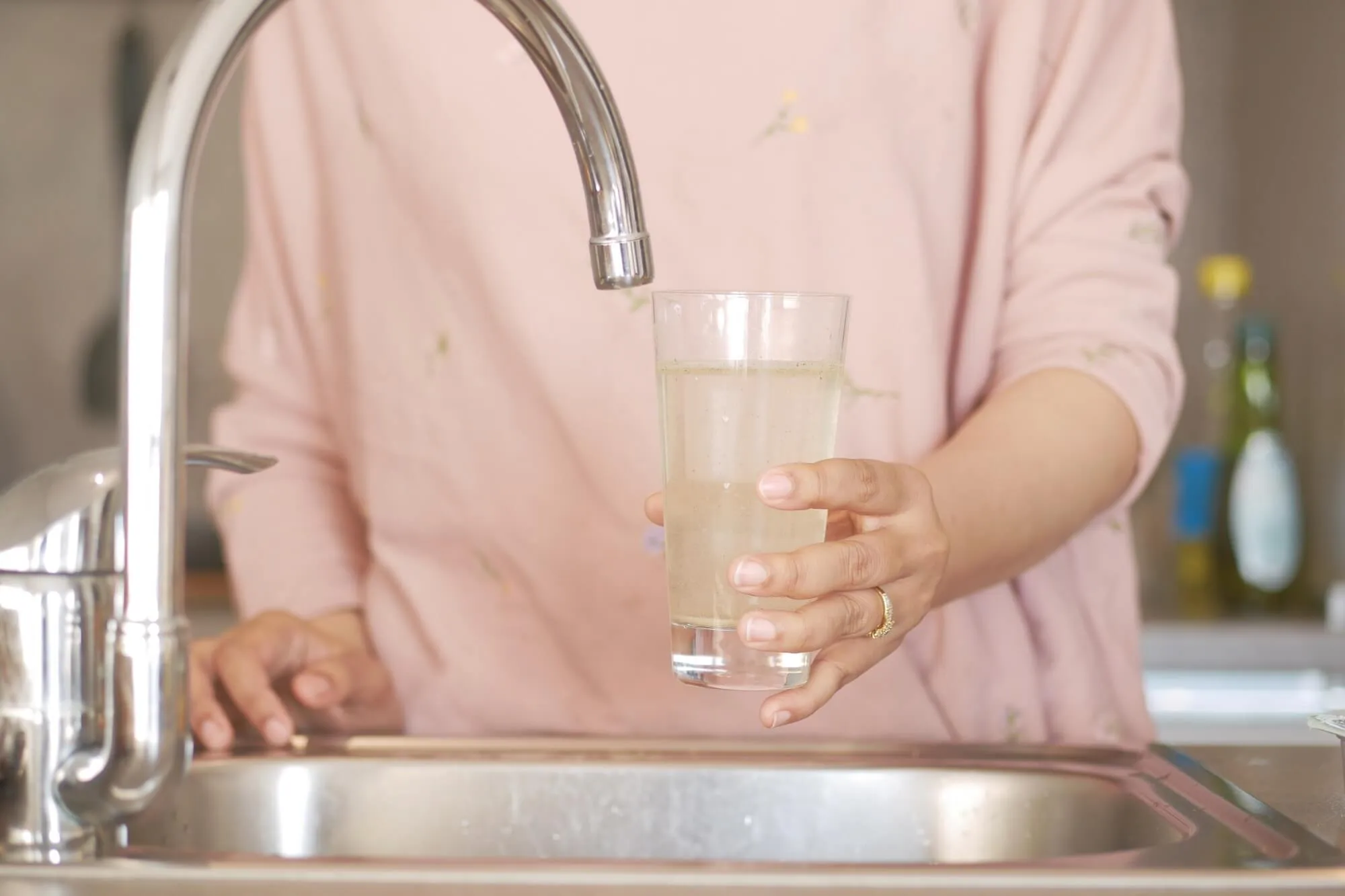 Person filling glass with dirty water from kitchen faucet.