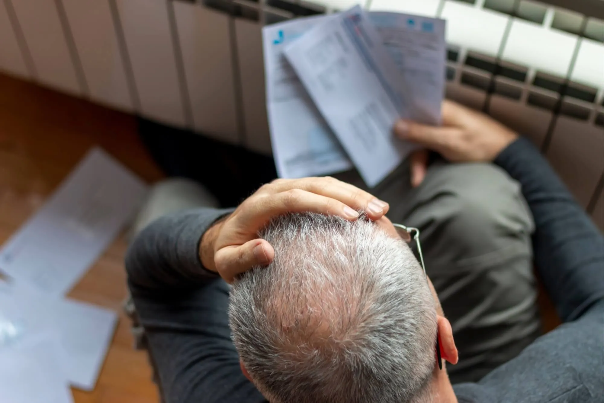 Man sitting on floor, overwhelmed, holding several bills in hand, surrounded by scattered envelopes.