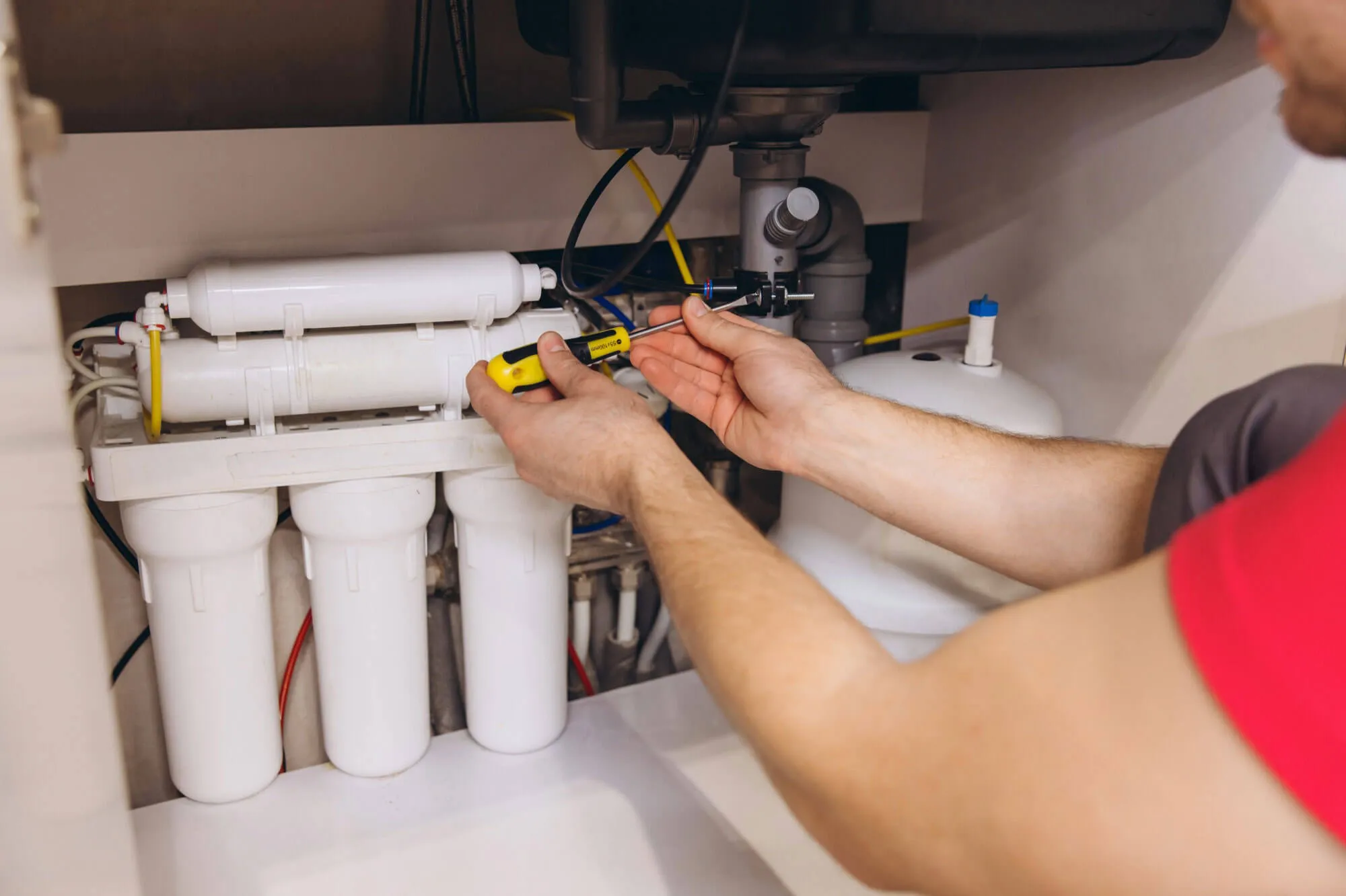 Person installing an under-sink water filtration system using a screwdriver.