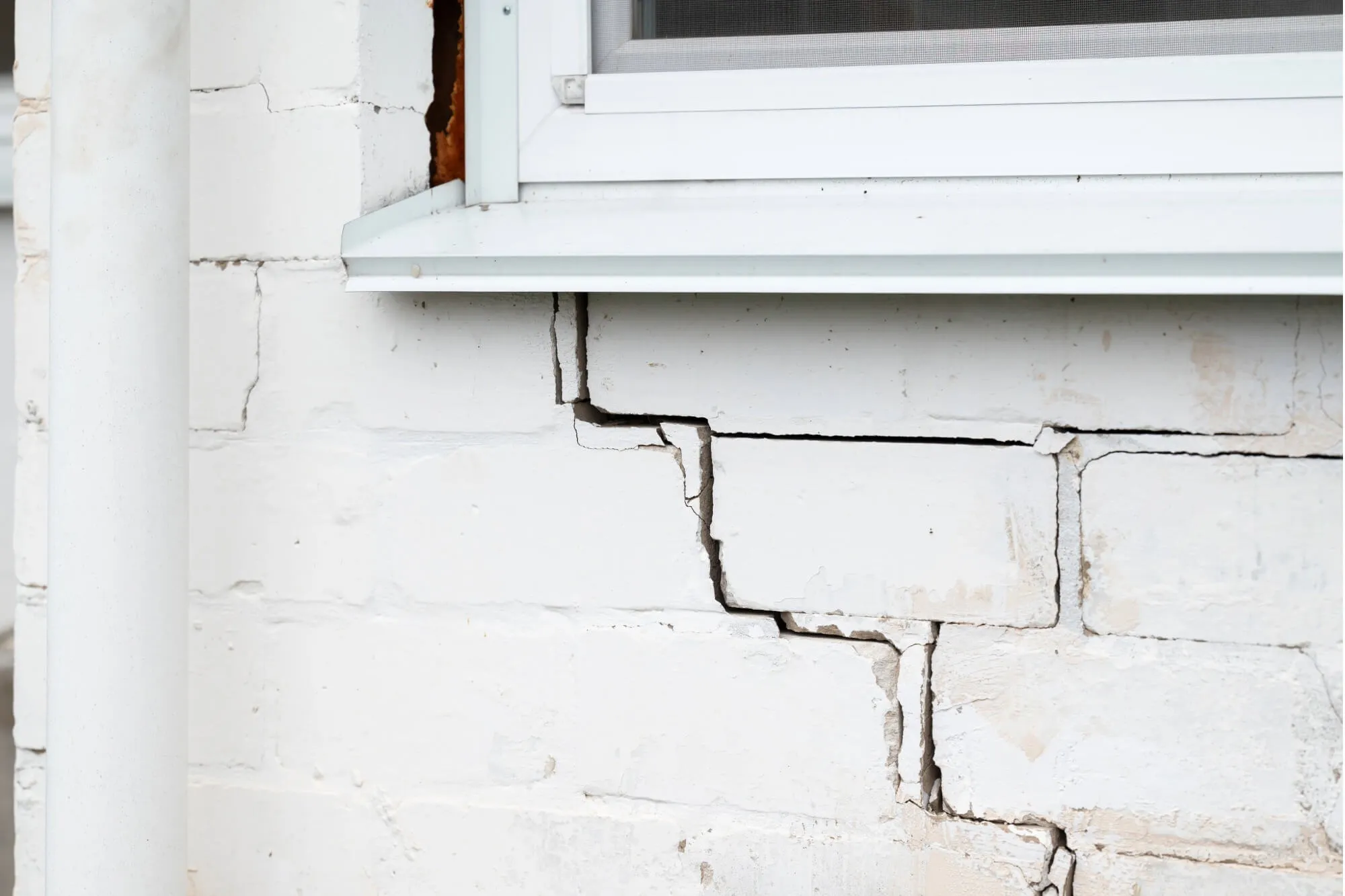 Cracked white brick wall near window, highlighting structural damage and home repair needs.