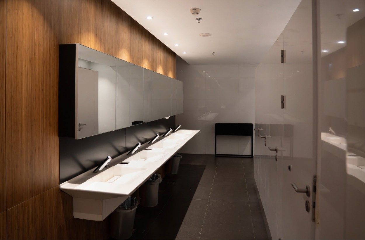 Modern public restroom with multiple sinks, mirrors, waste bins, and a wooden accent wall.