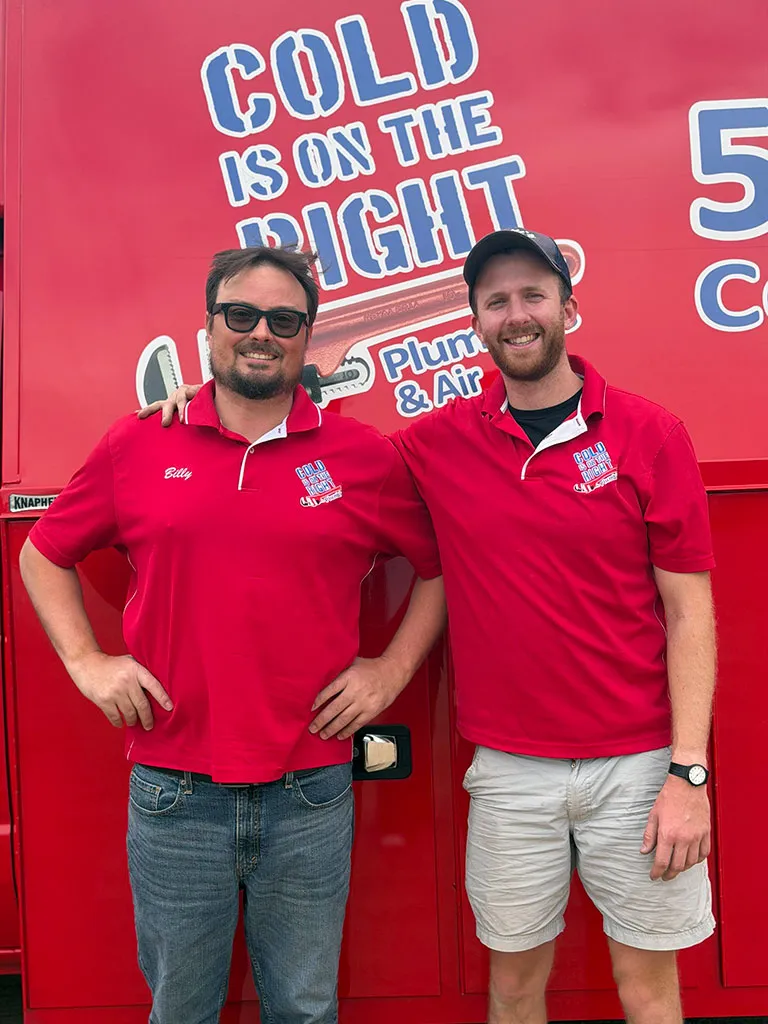 Two men wearing matching red shirts with Cold Is On The Right Plumbing & Air logos posing in front of a red vehicle with company branding.