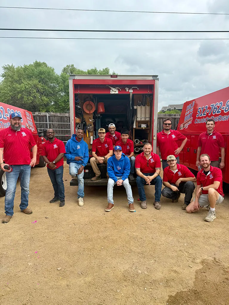 Group of twelve men in red and blue shirts posing in front of an open red service truck and red service van with work equipment inside.