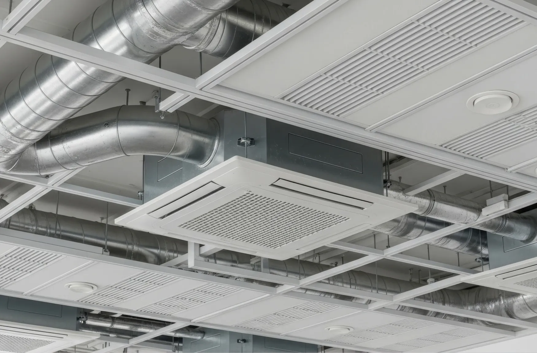 Ceiling-mounted HVAC duct system with metal air ducts and air vents in a commercial building.