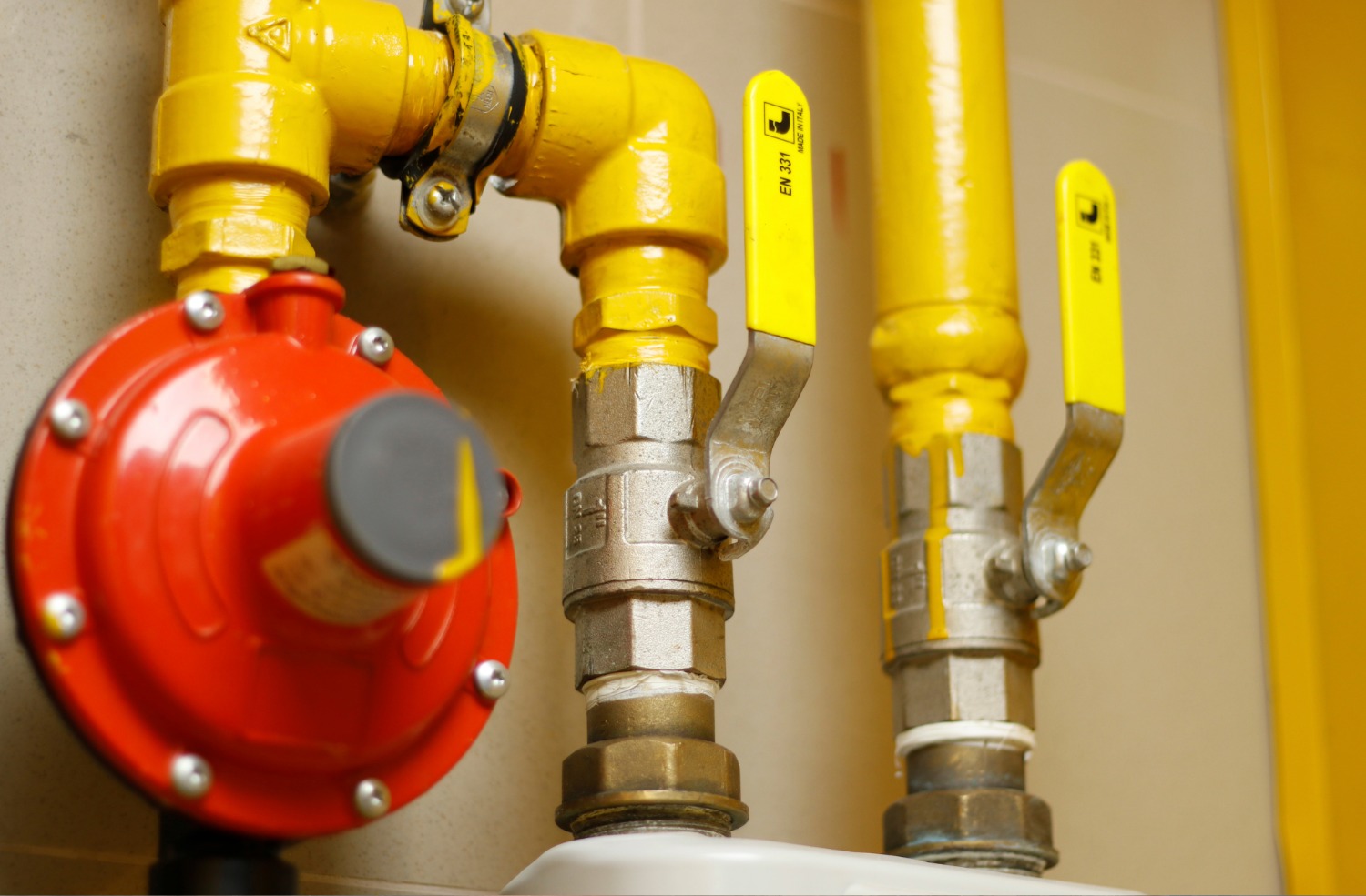 Close-up of yellow gas pipes with yellow valve handles and a red pressure regulator attached.
