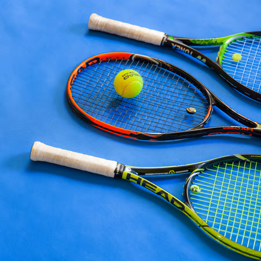 Drei professionelle Tennisschläger auf blauem Untergrund mit einem Tennisball.