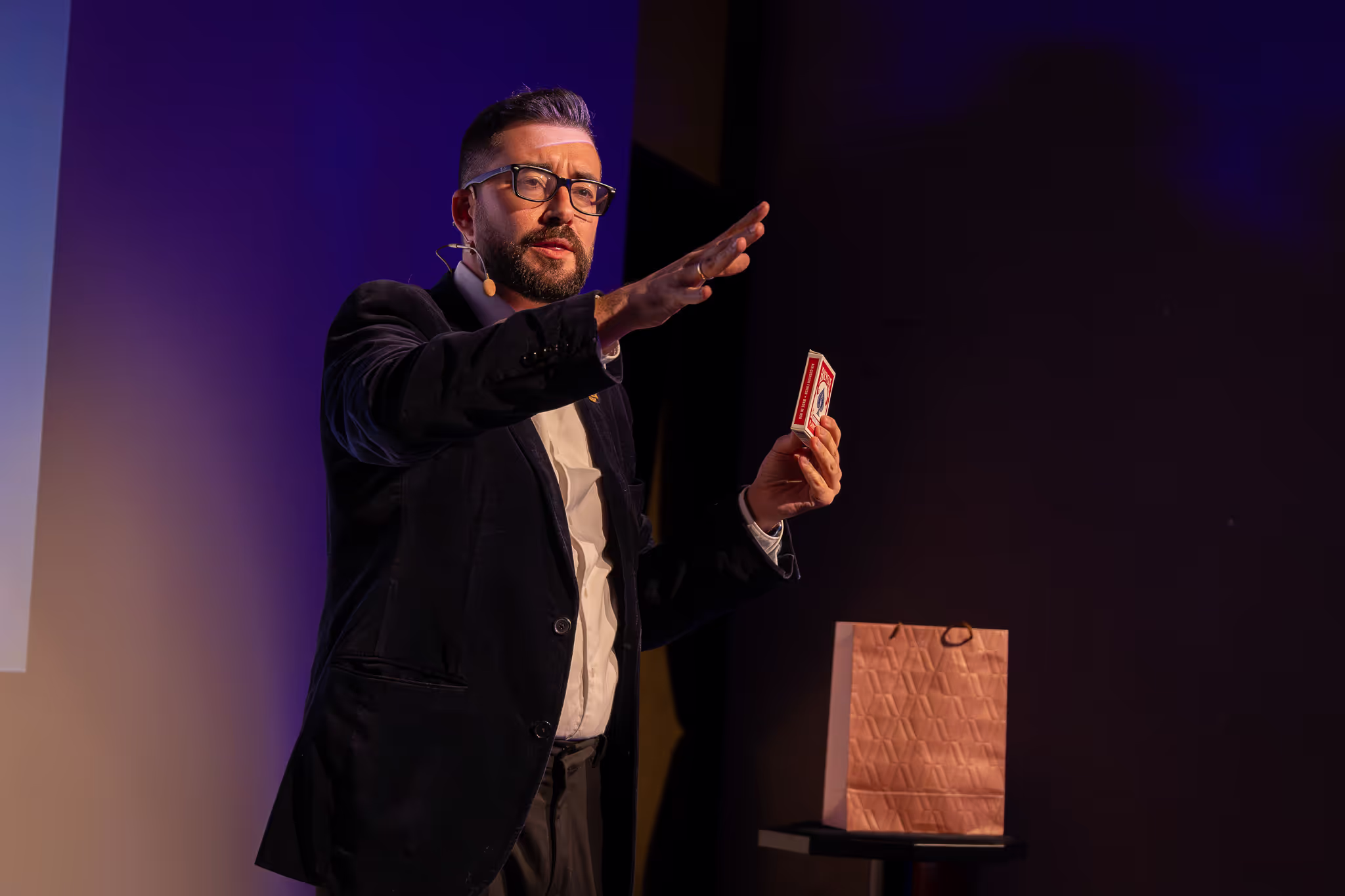 Mago haciendo espectaculo de magia desde el escenario con cartas y una prediccion en una bolsa