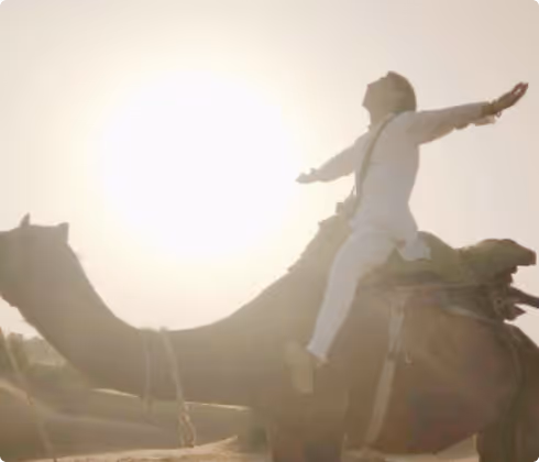 Yuki, our founder, joyfully sits on a camel in a sunlit desert.