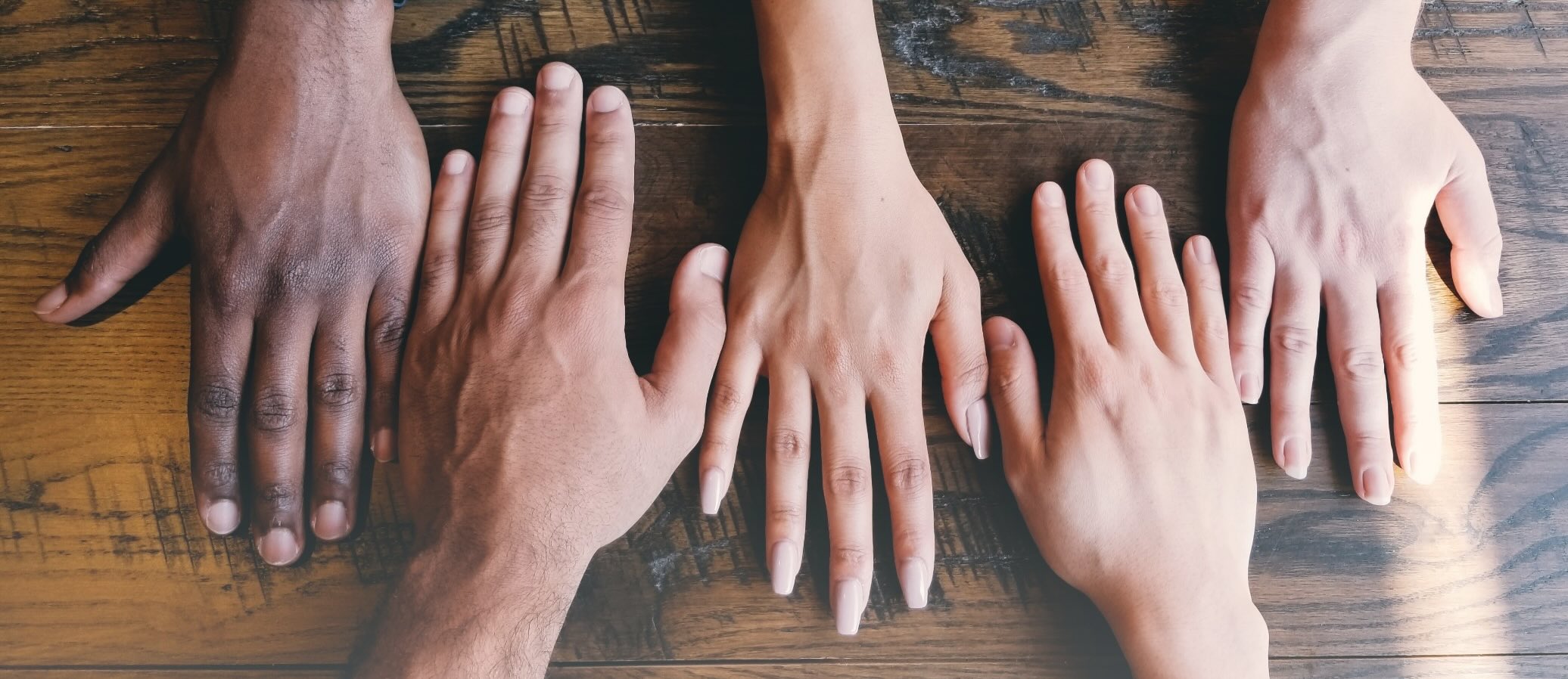 木のテーブルの上に並べられた多様な手が、団結とチームワークを象徴している。