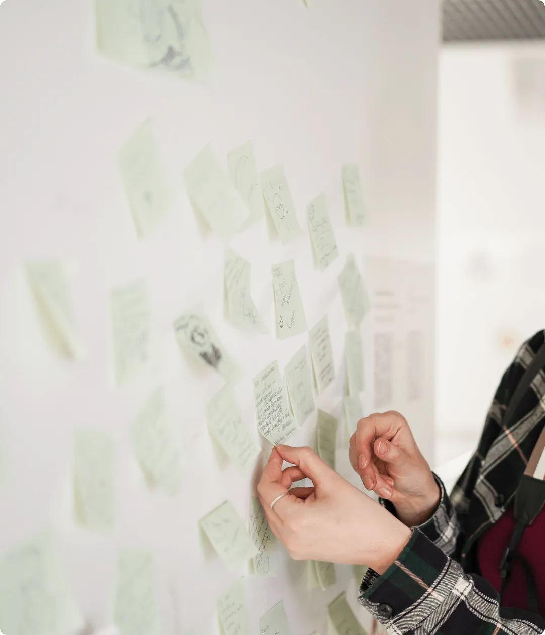 手書きのアイデアが書かれた付箋を壁に貼る人。ユーザー分析とインサイト収集を含むリサーチフェーズを象徴。