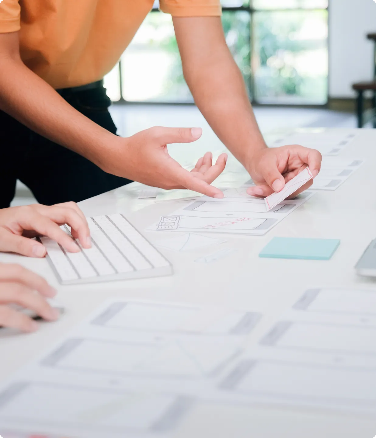 スケッチや図が描かれた紙をテーブルに広げ、指差す人。さまざまなアイデアやソリューションを検討するアイディエーションフェーズを表現。