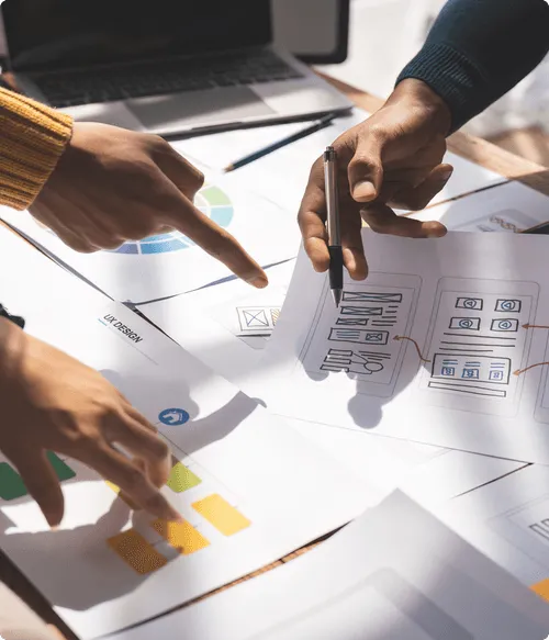 デスクで印刷されたチャートやワイヤーフレームスケッチを分析し、デザインソリューションの仮説立案に取り組む複数の人々。