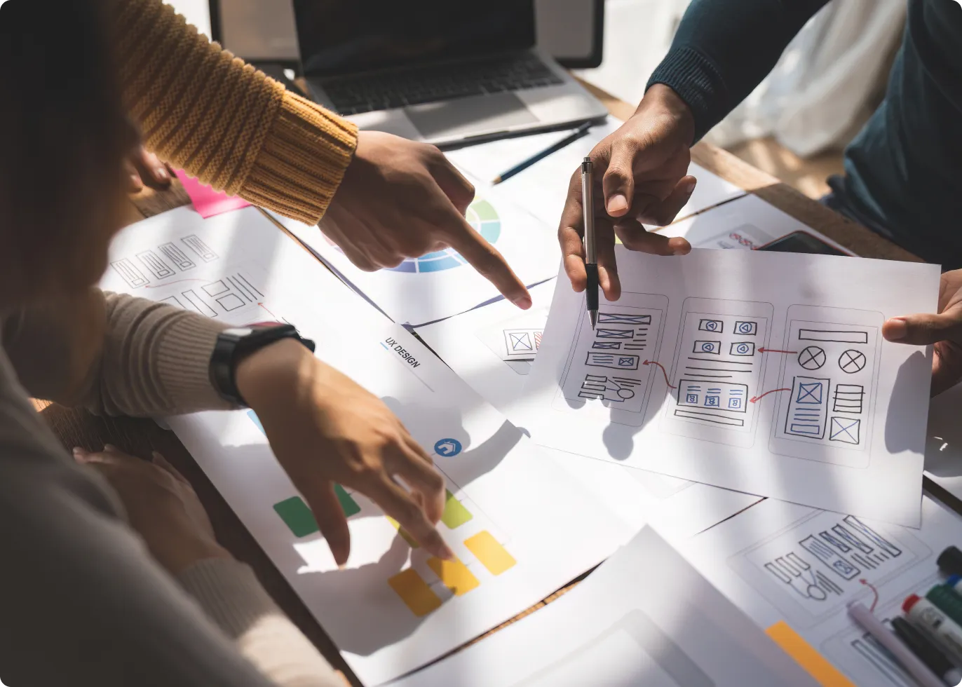 デスクで印刷されたチャートやワイヤーフレームスケッチを分析し、デザインソリューションの仮説立案に取り組む複数の人々。