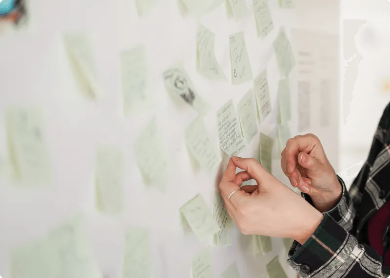 手書きのアイデアが書かれた付箋を壁に貼る人。ユーザー分析とインサイト収集を含むリサーチフェーズを象徴。