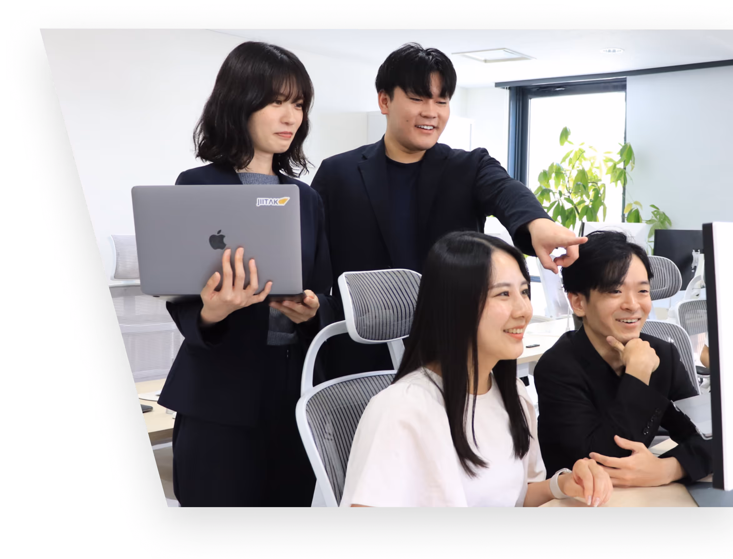 近代的なオフィスで笑顔でアイデアを話し合う多様なチーム。タブレットとパソコンを使用。