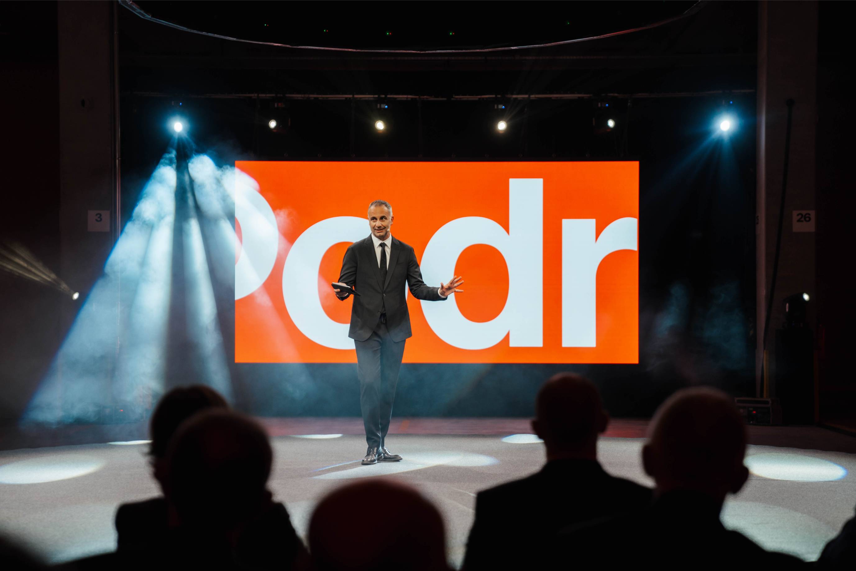 Otvorenje Podravkina distribucijskog centra: govornik pred velikim narančastim LED ekranom, reflektori i publika