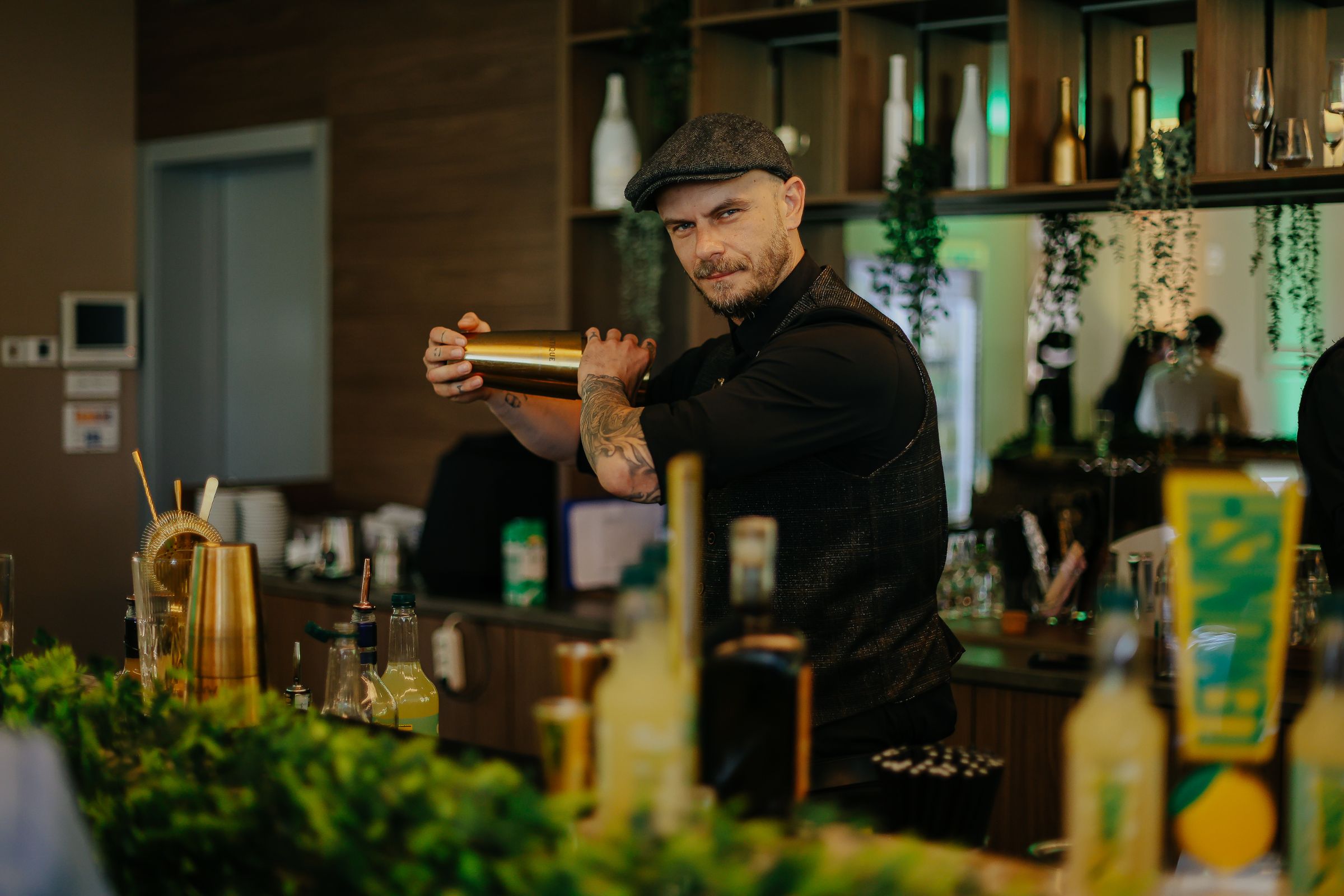 Lemonish lansiranje: barmen mućka koktel zlatnim shakerom za šankom ukrašenim zelenilom i Lemonish oznakama