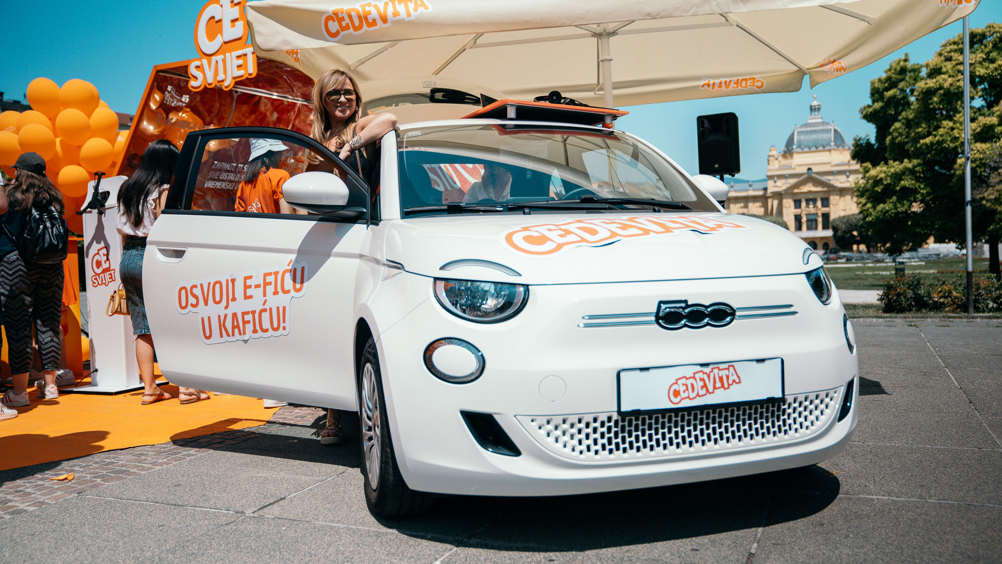 Cedevitaskop: bijeli električni automobil s natpisom 'Osvoji e-ficu u kafiću!', iza njega CE svijet kaleidoskop