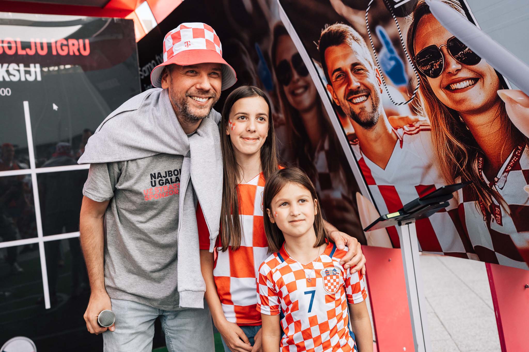 Voditelj s mikrofonom pozira s dvije mlade navijačice u kockastim dresovima Hrvatske u HT Football Fun Zoneu