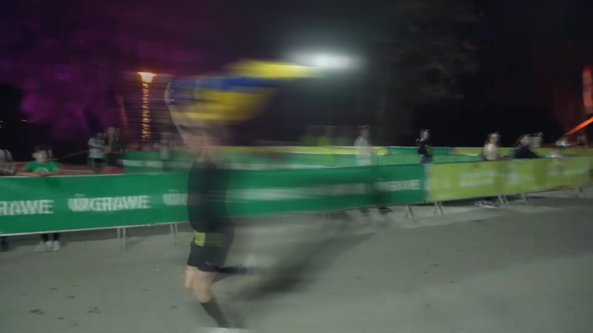 GRAWE Noćni maraton na Bundeku: trkač juri pokraj zelenih GRAWE ograda u noći dok gledatelji prate utrku