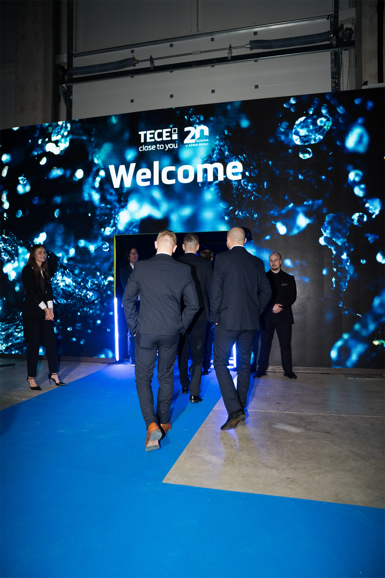Gosti u odijelima hodaju plavim tepihom prema LED zidu s natpisom Welcome i logom TECE 20 godina