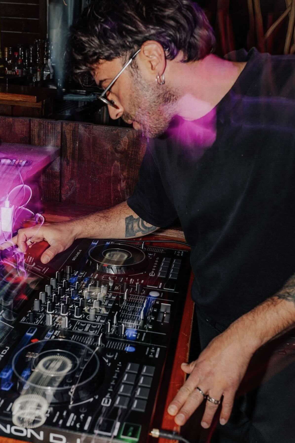 DJ steht hinter beleuchtetem DJ-Pult mit grünem Licht und abstraktem Hintergrund