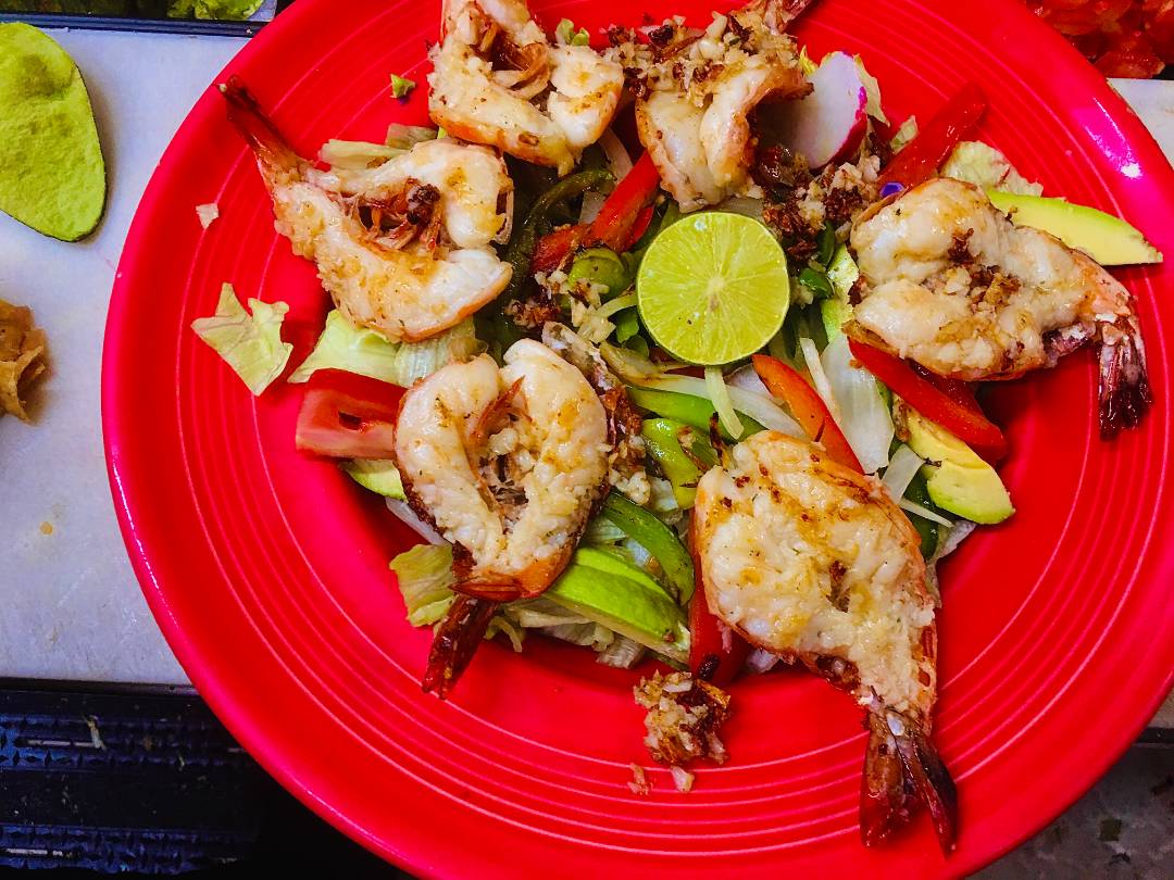 Shrimp on a red plate served with greens.