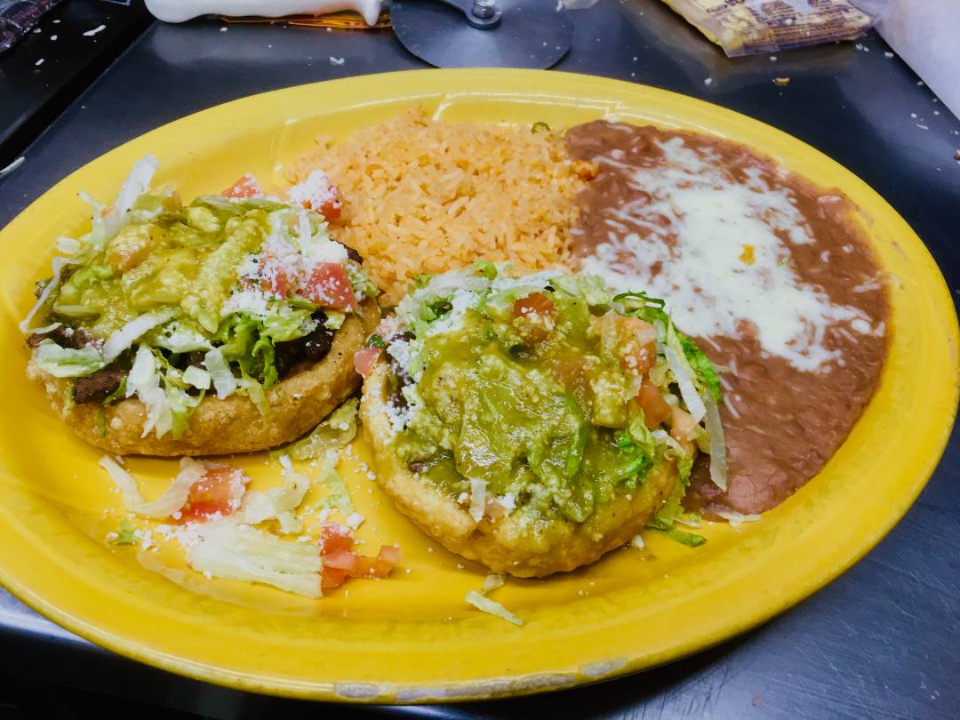 A plate featuring two sopes and a serving of rice and beans beside them.