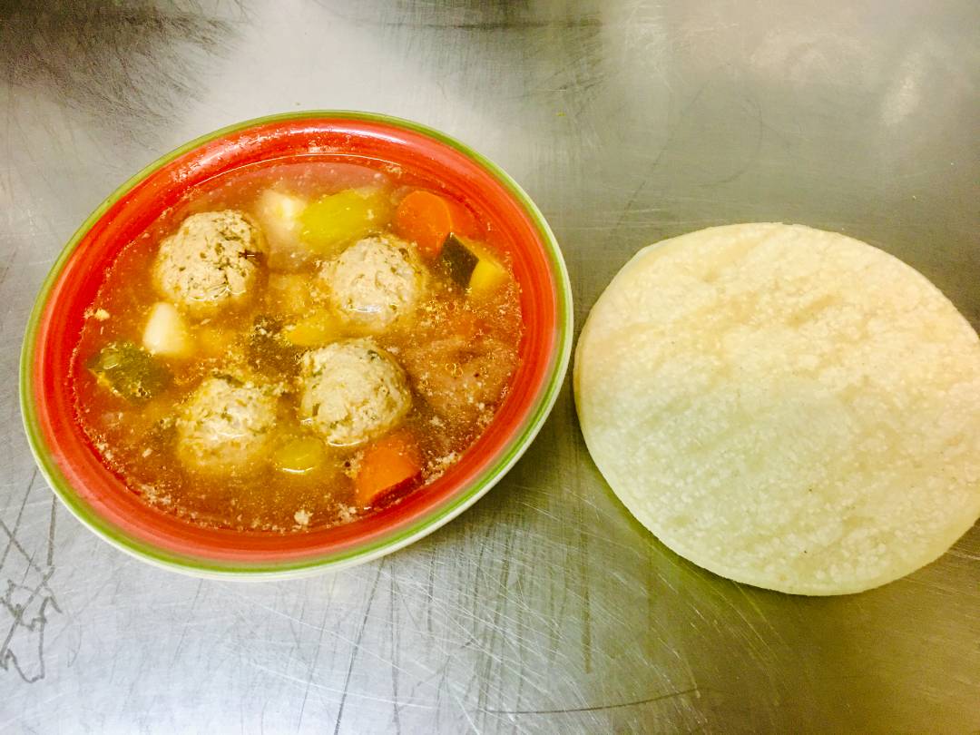 A bowl of steaming soup beside a flour tortilla.