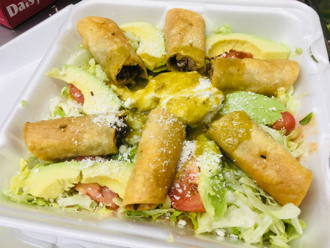 A plate of flautas on top of lettuce, avocado and tomato, topped with grated cheese