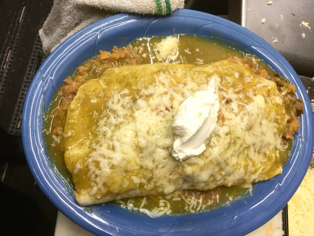 A plate of enchiladas topped with melted cheese and a dollop of sour cream, garnished with fresh herbs.